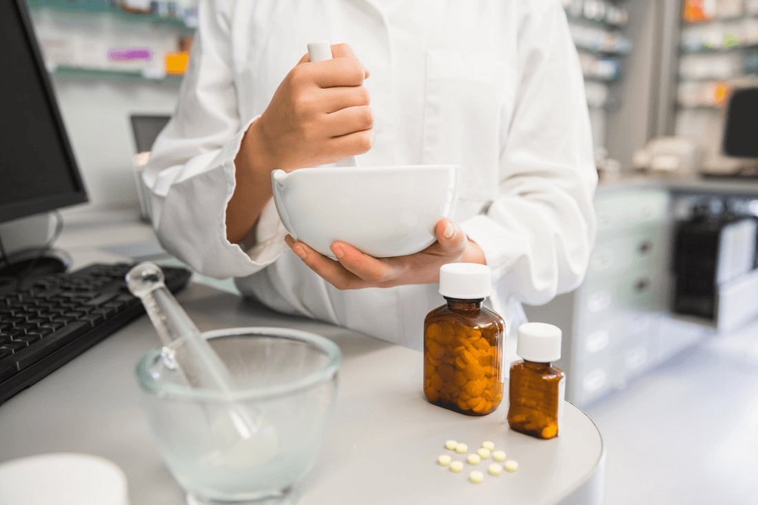 Pharmacist using mortar and pestle with medication bottles
